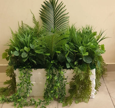 Artificial Plant Combo in Rectangle Pot Plants UAE. Assorted green plants in a white container on a light-colored floor.
