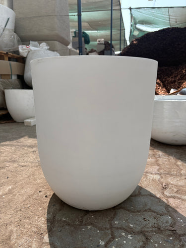 White Arco Fiber Pot with Matte Finish and Lifetime Warranty, UAE. Close-up of a white ceramic vase against a textured stone wall.
